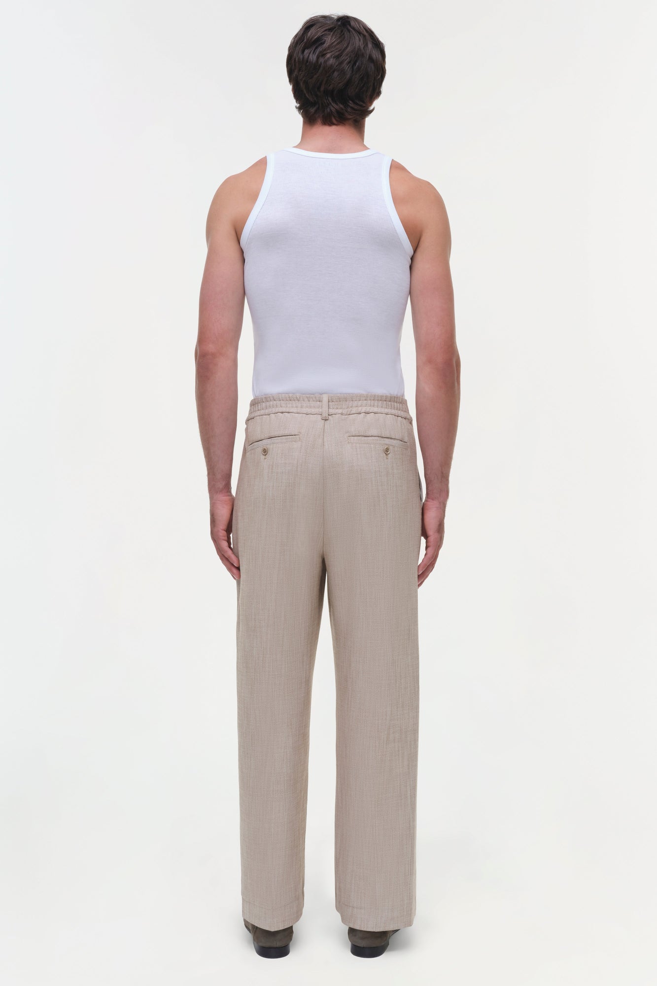 Beige textured pants with flat front and button closure, shown from back view on model wearing white tank top.