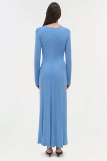 Woman wearing a blue draped jersey midi dress with long sleeves, shown from back view.