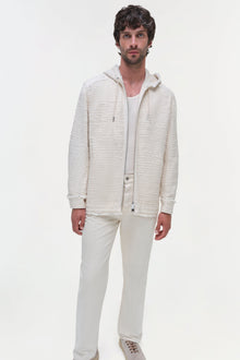 Man wearing cream textured zip-up hoodie jacket with white pants and sneakers.