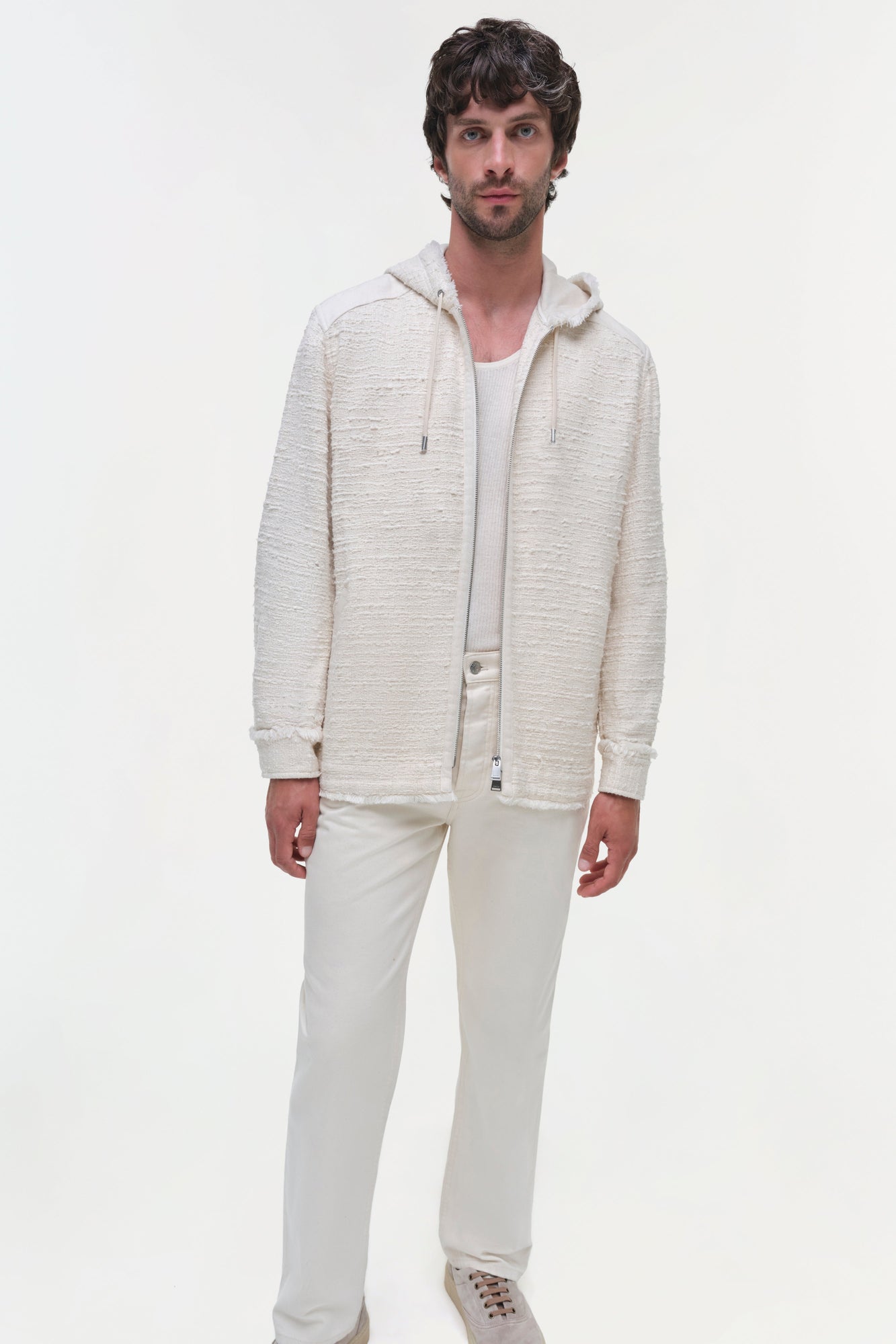 Man wearing cream textured zip-up hoodie jacket with white pants and sneakers.