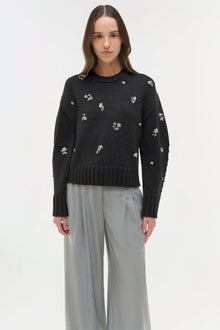 Black knit crewneck sweater with white floral embellishments scattered across the chest and sleeves.