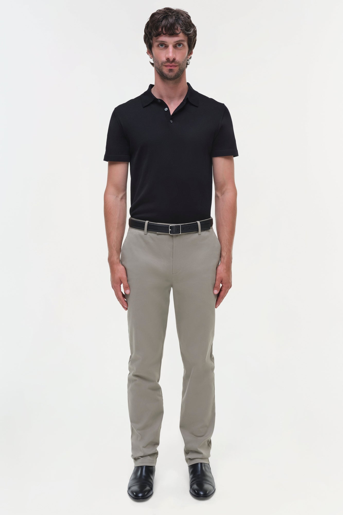Man wearing black polo shirt and beige cotton twill trousers with belt and black shoes.