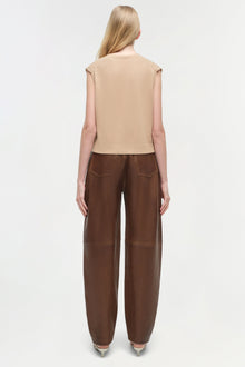 Beige sleeveless cashmere vest worn over pink long-sleeve shirt, paired with brown leather pants.
