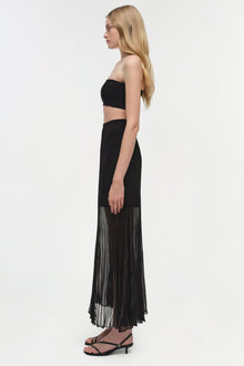 Black knit bralette with bandeau style and thin straps, worn with pleated skirt.