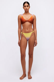 Woman wearing orange bikini top with center tie detail and yellow-to-purple ombre bikini bottom.