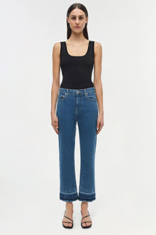 Woman wearing blue straight-leg jeans with frayed hem and black sleeveless tank top.