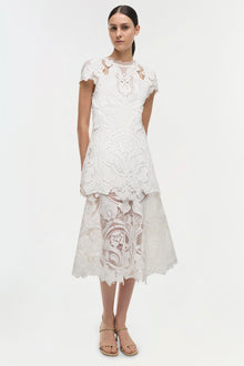 White lace dress with short sleeves, patterned cutout details, and layered midi skirt with scalloped hem.