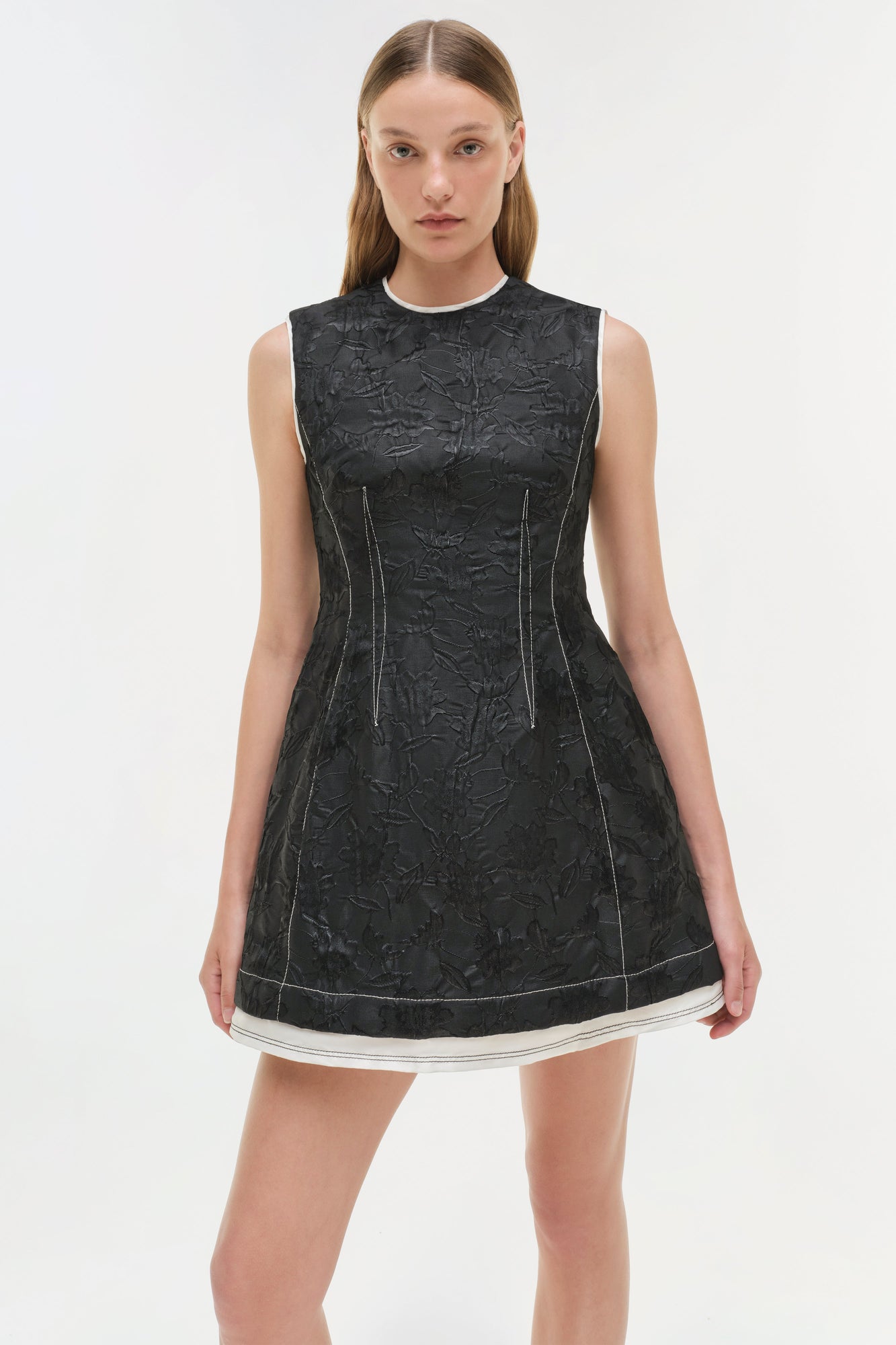 Black jacquard sleeveless mini dress with textured pattern, white trim at hem, and visible seam details.