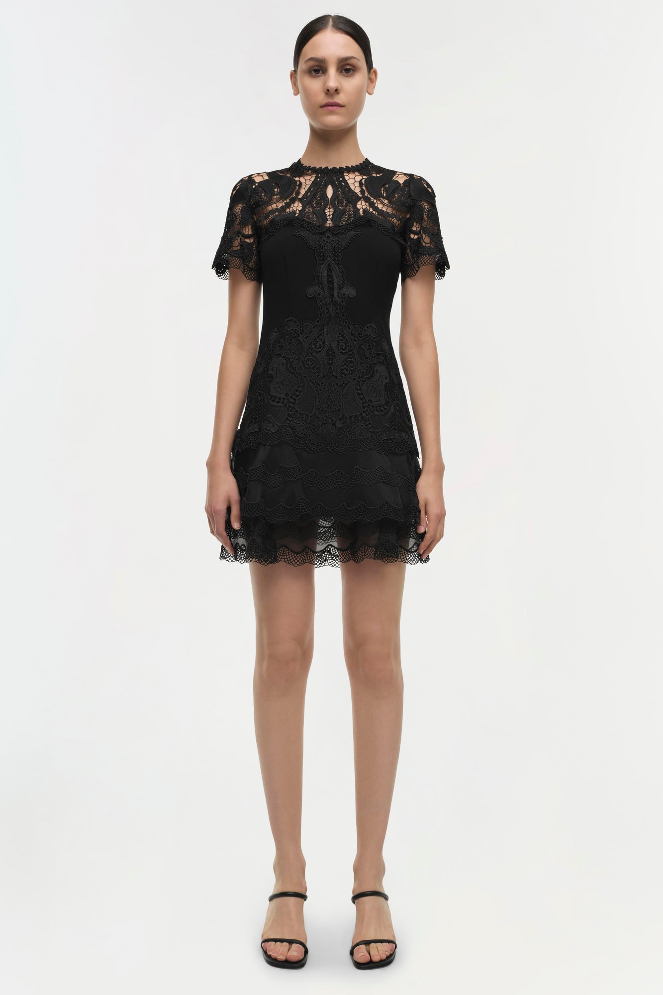 Black lace dress with short sleeves and layered paisley pattern detail throughout, worn with black strappy sandals.