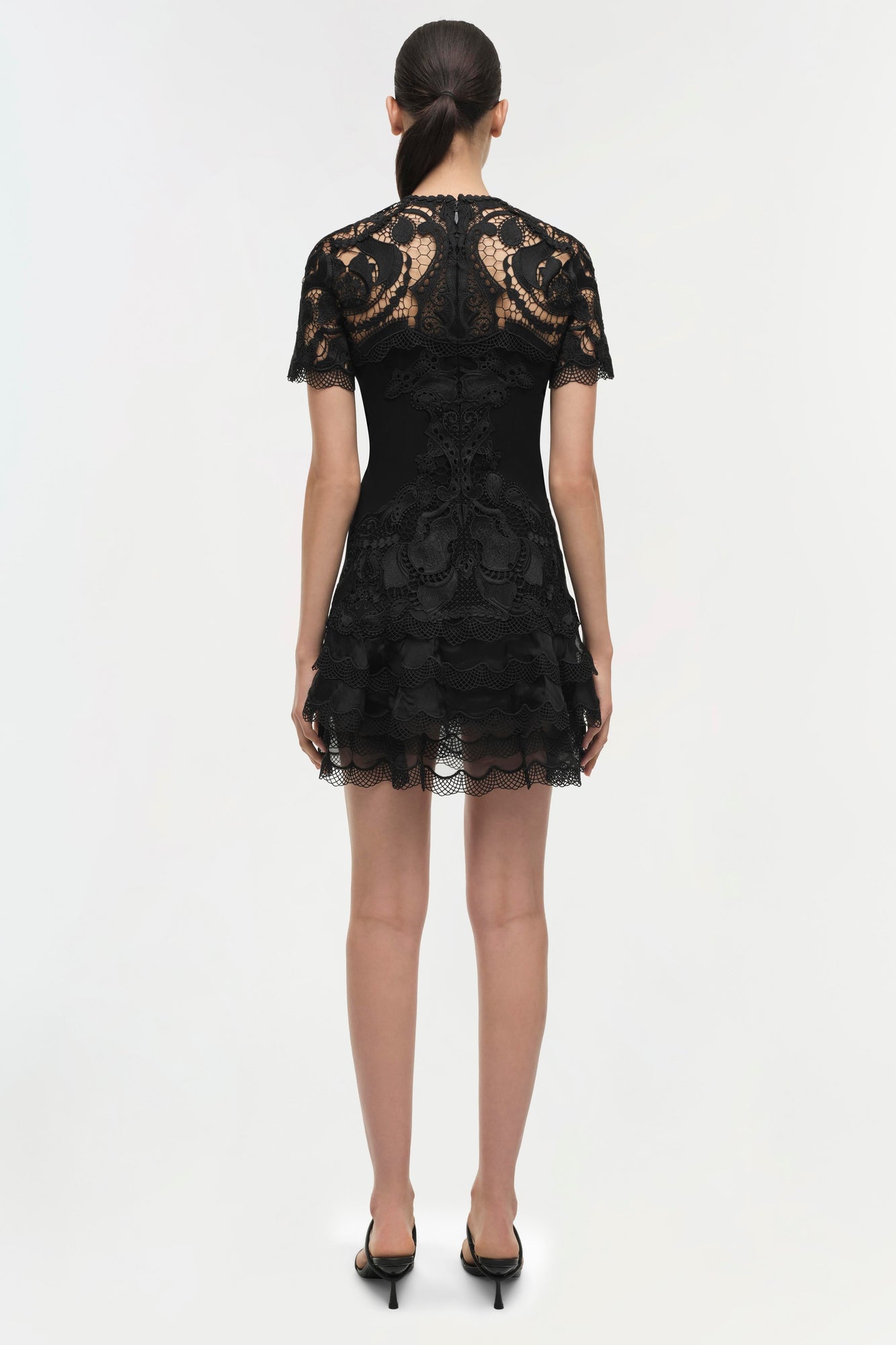 Black lace short dress with short sleeves and tiered hemline, shown from back view on model.