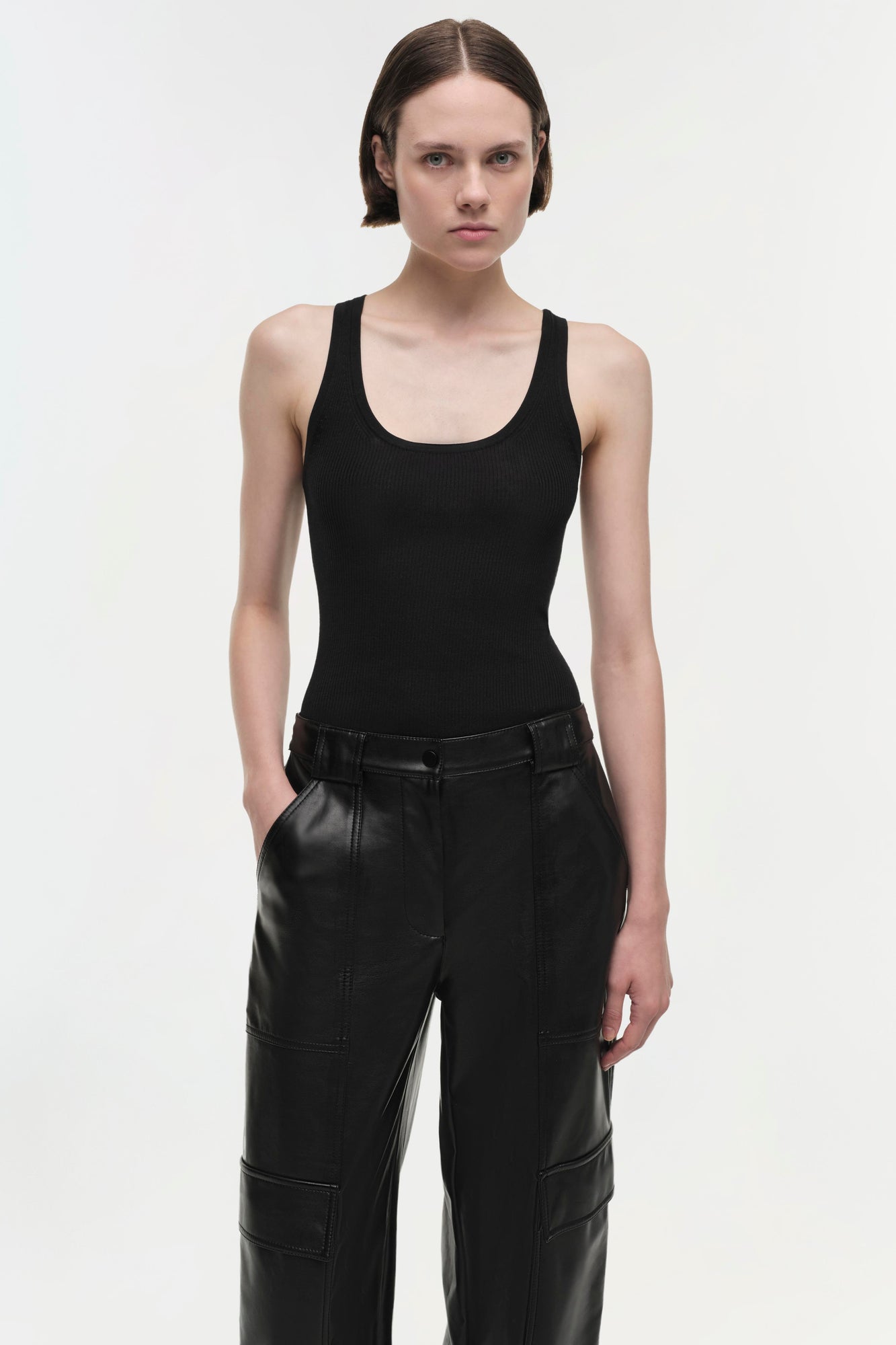 Black leather cargo pants with visible seam panels and belt loops, worn with a black ribbed tank top.