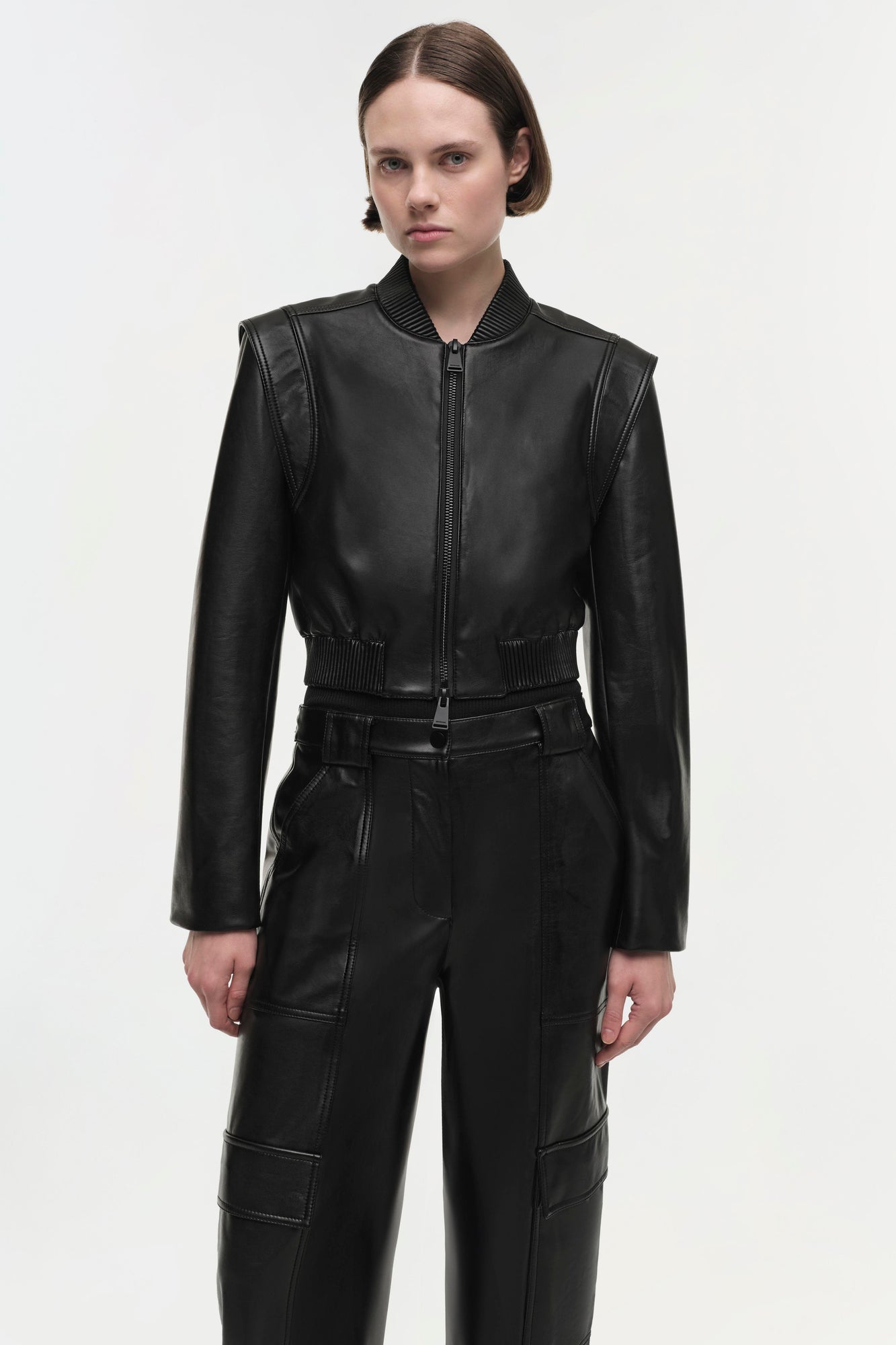 Black leather cropped jacket with ribbed collar and cuffs, front zip closure, and contrast stitching details.