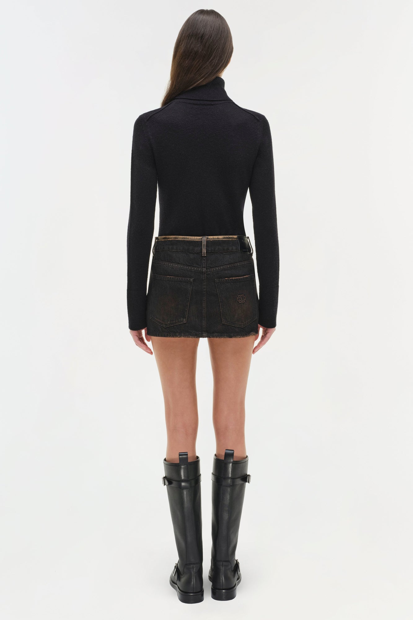 Woman wearing a black turtleneck and dark denim mini skirt with back pockets, paired with black boots.
