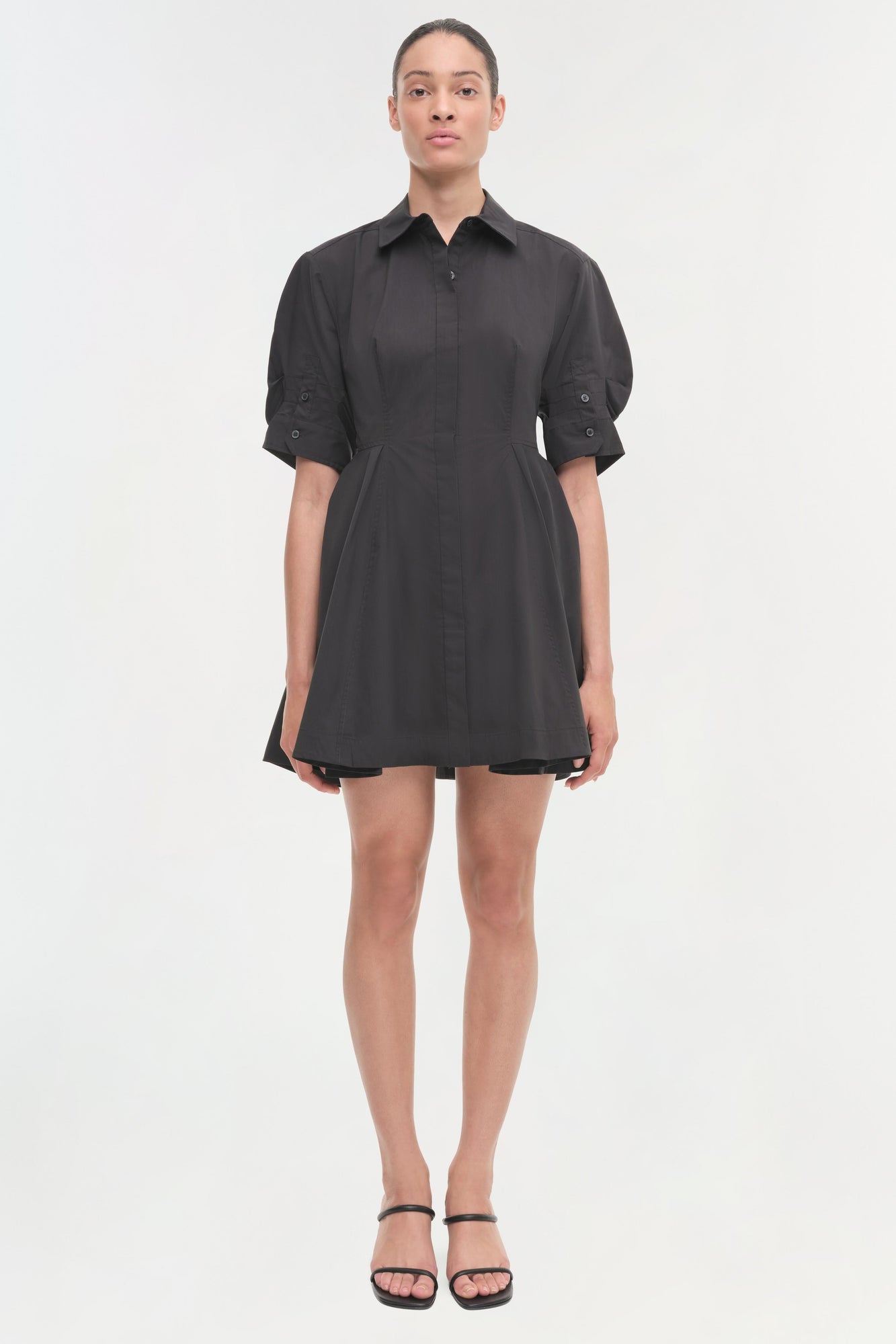 Black button-front shirt dress with puffed sleeves and fitted waist, shown on model wearing black sandals.