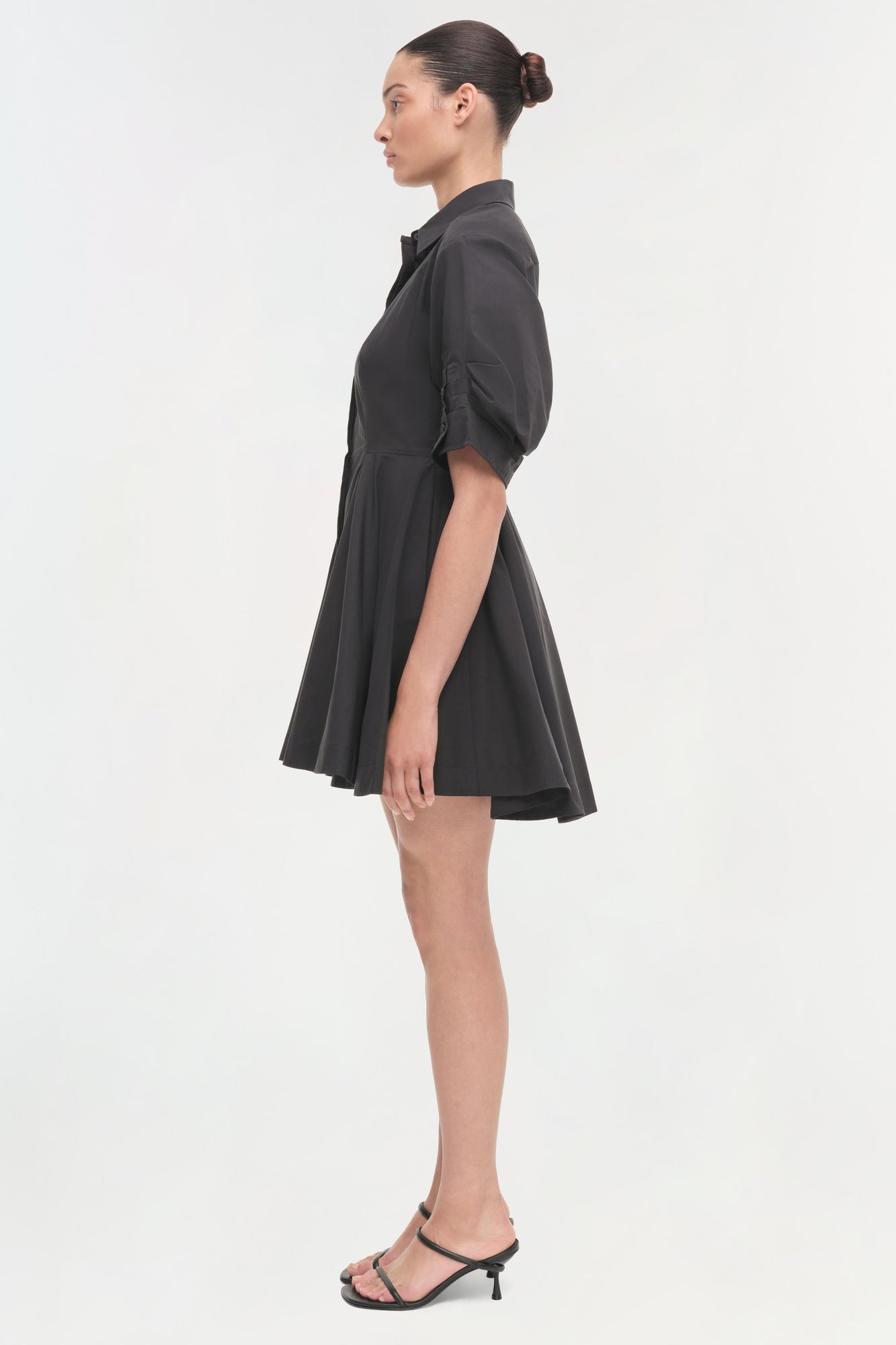 Black collared shirt dress with puffed sleeves and full skirt, shown on model in side profile.