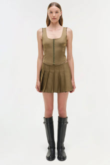 Olive green pleated mini skort with matching sleeveless tank top and black knee-high boots.
