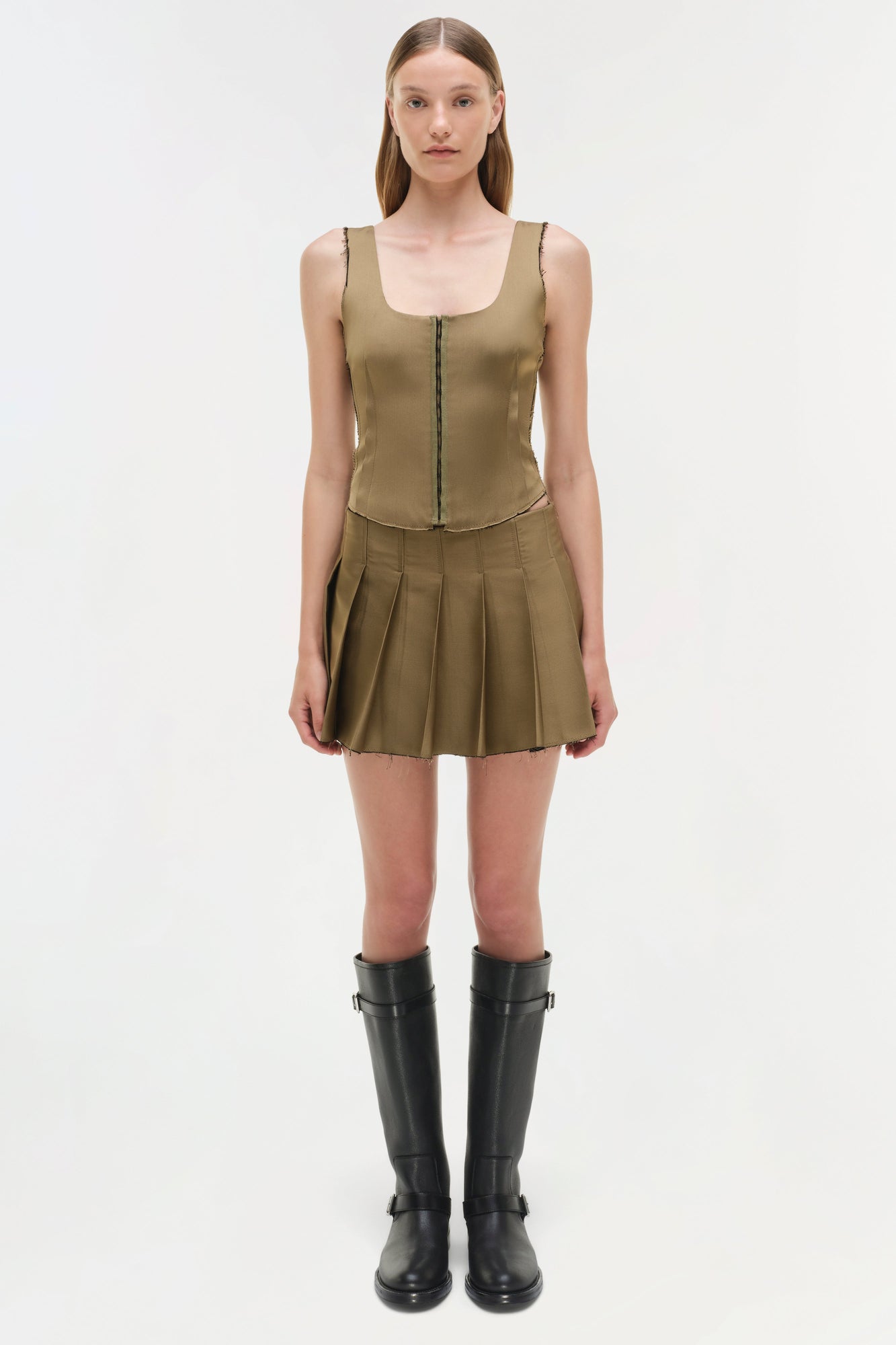 Olive green pleated mini skort with matching sleeveless tank top and black knee-high boots.