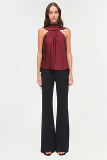Burgundy satin halter top with draped cape collar and black flared pants.