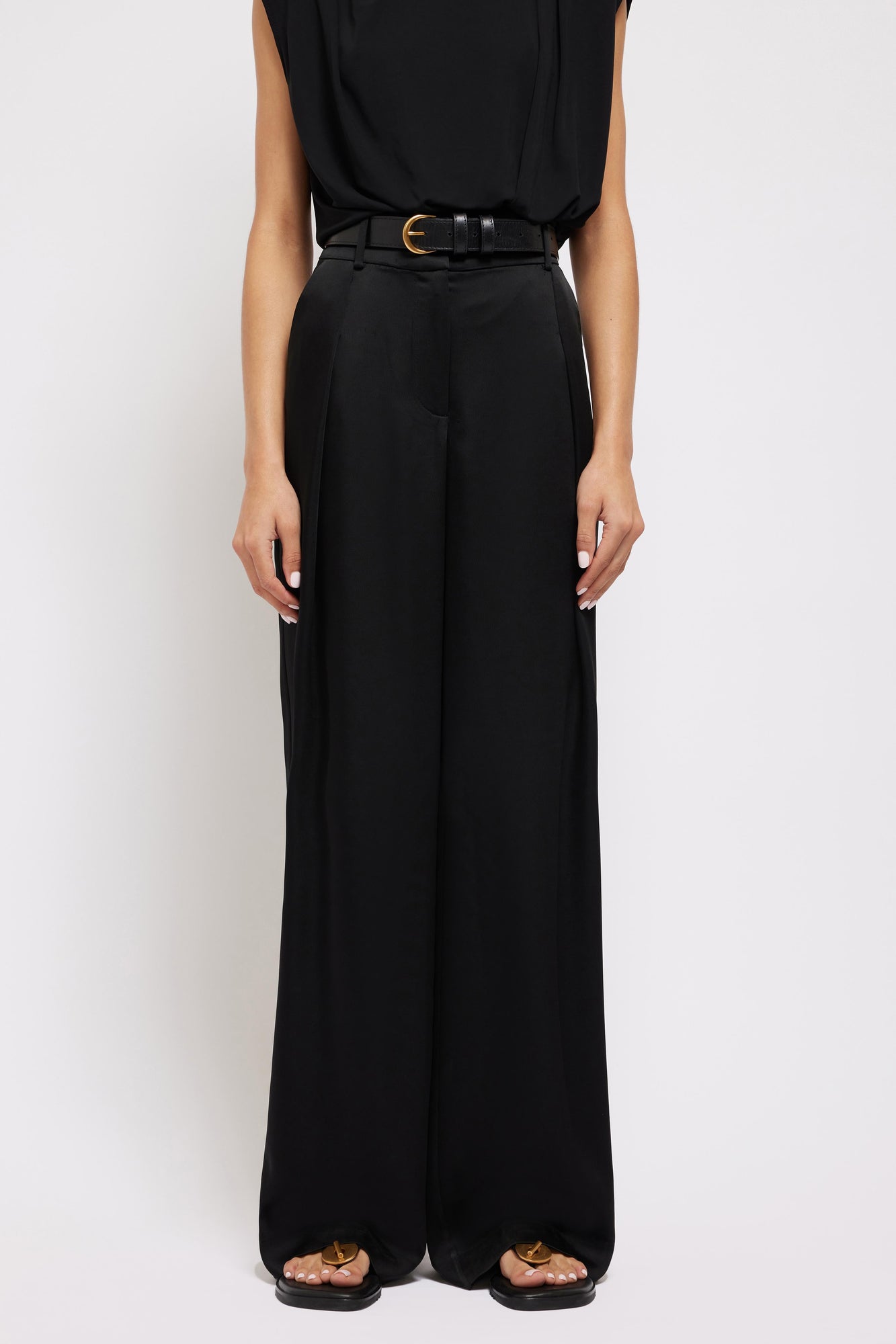 Black wide-leg pants with pleated front, gold buckle belt, and full-length straight silhouette.