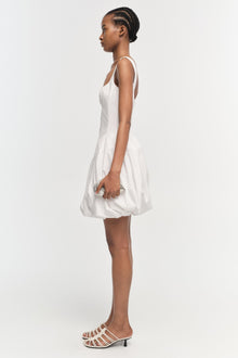 White sleeveless mini dress with gathered skirt, shown on model in side profile view.