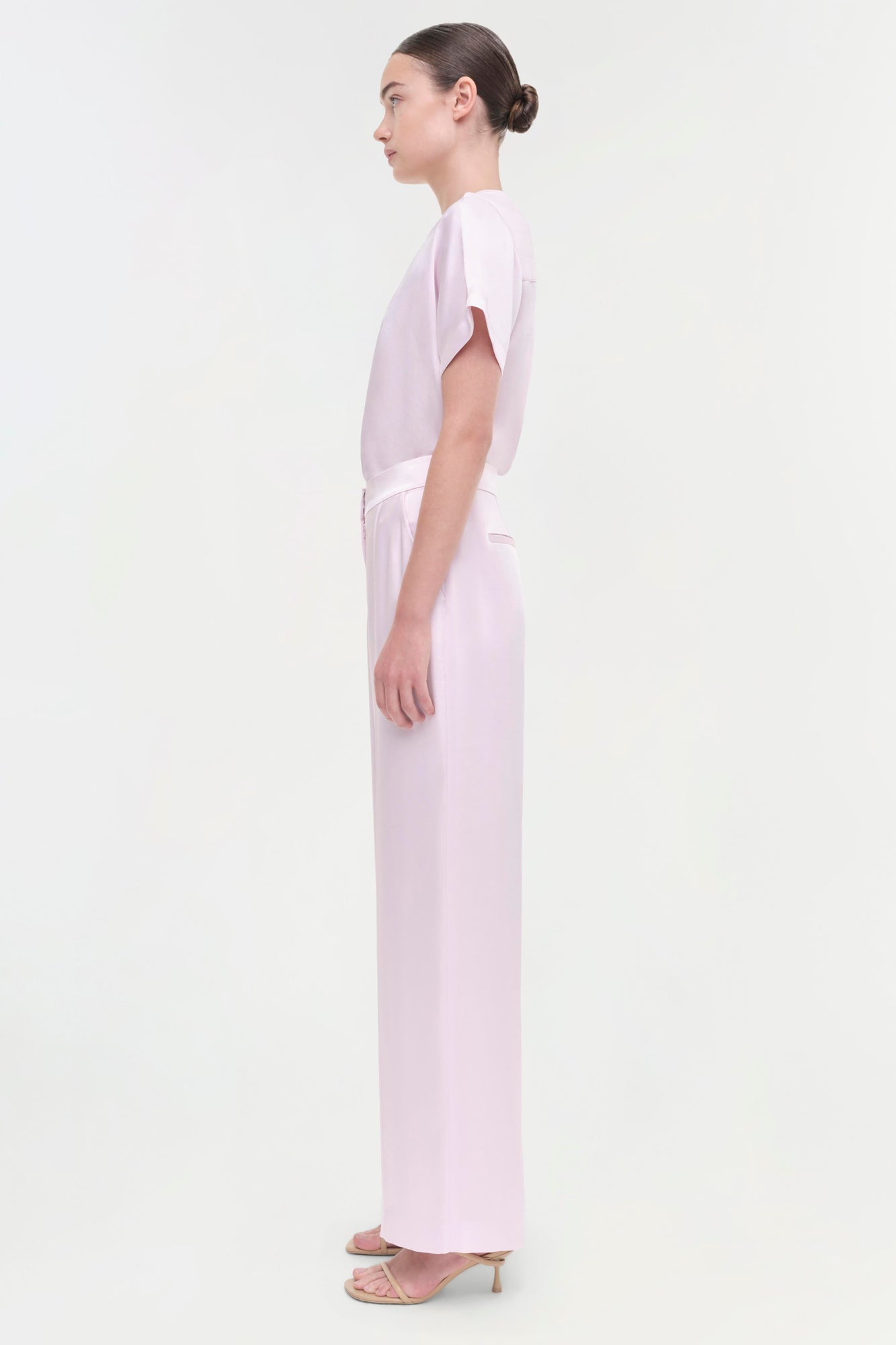 Woman wearing light pink wide-leg pants with a matching short-sleeve top, shown in profile view.