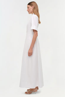 Woman wearing a white cotton shirt dress with short sleeves and an A-line skirt, shown in profile view.