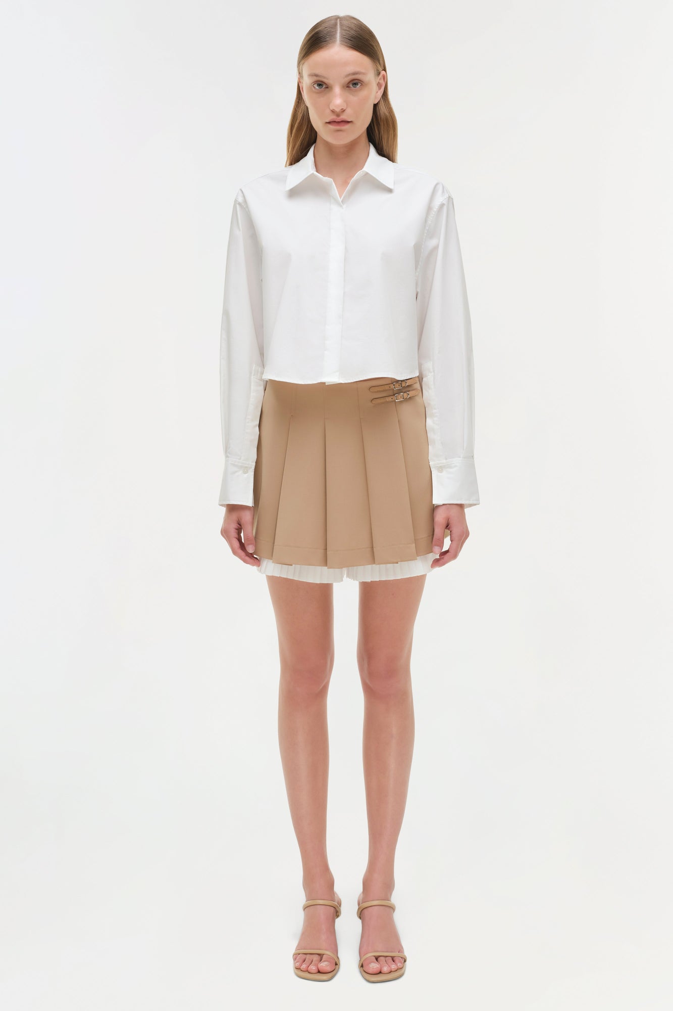 Beige pleated skort with white hem trim, styled with white button-up shirt and tan sandals.