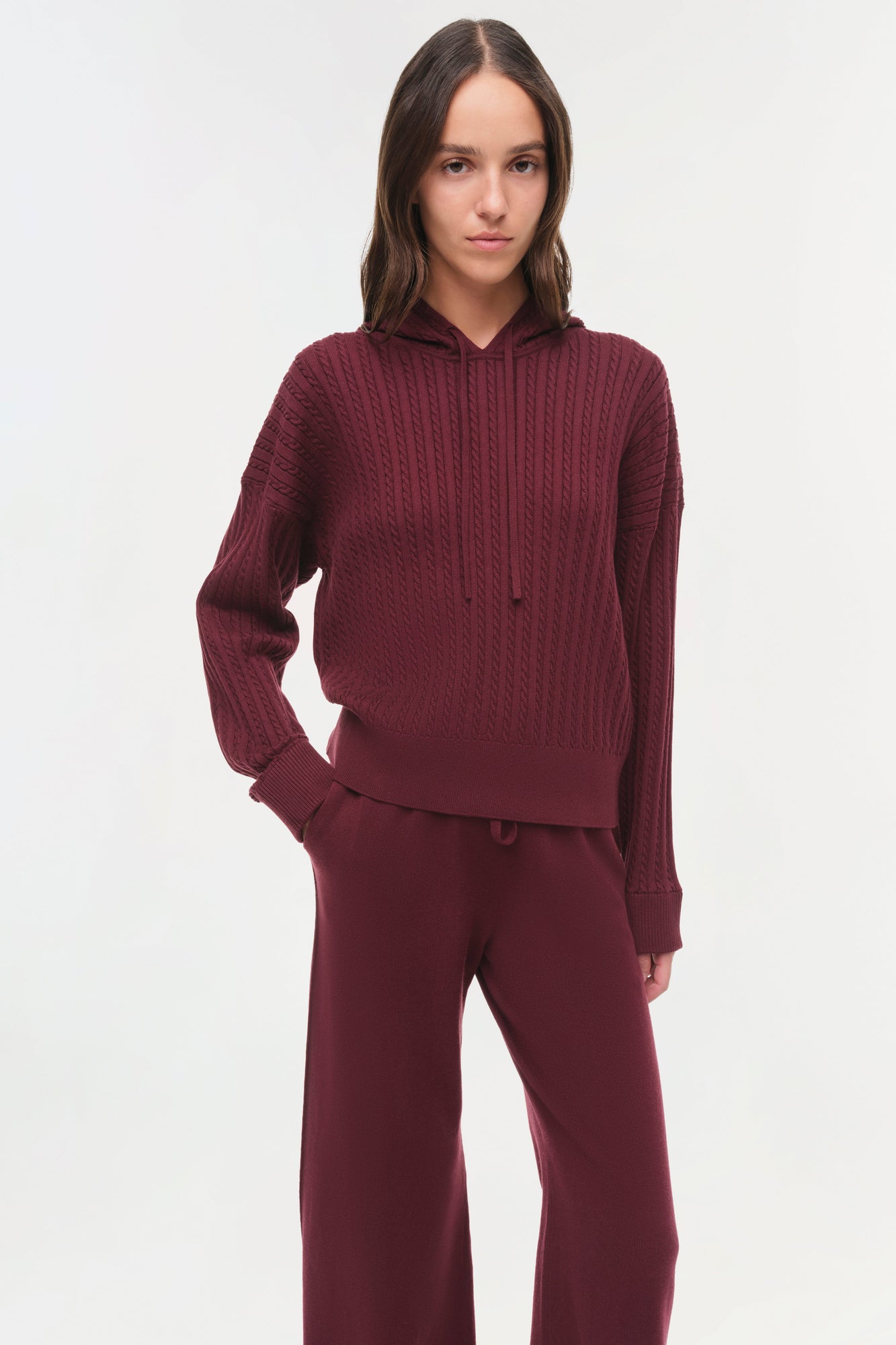 Woman wearing burgundy cable-knit hoodie and matching wide-leg pants against white background.
