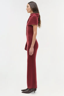 Woman wearing burgundy midi dress with draped shoulder detail and black kitten heels, shown in profile.