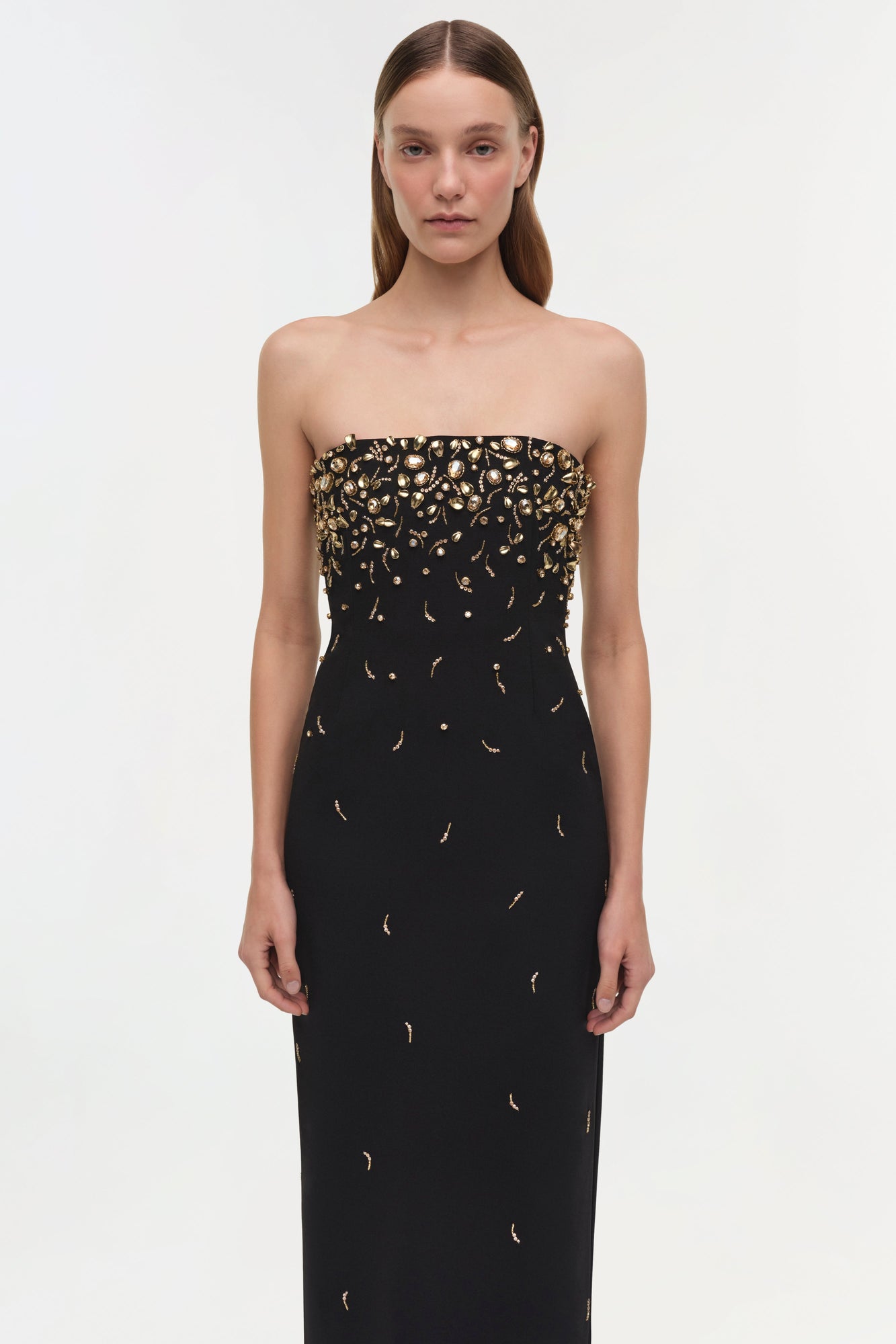 Black strapless gown with gold beaded embellishments concentrated at neckline, worn by model with long brown hair.