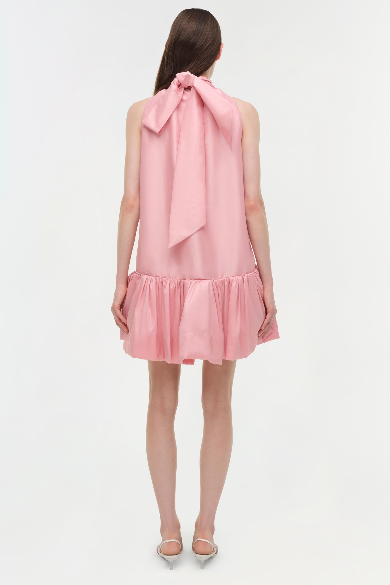 Pink sleeveless mini dress with bow tie neckline and gathered ruffle hem, shown from back view.