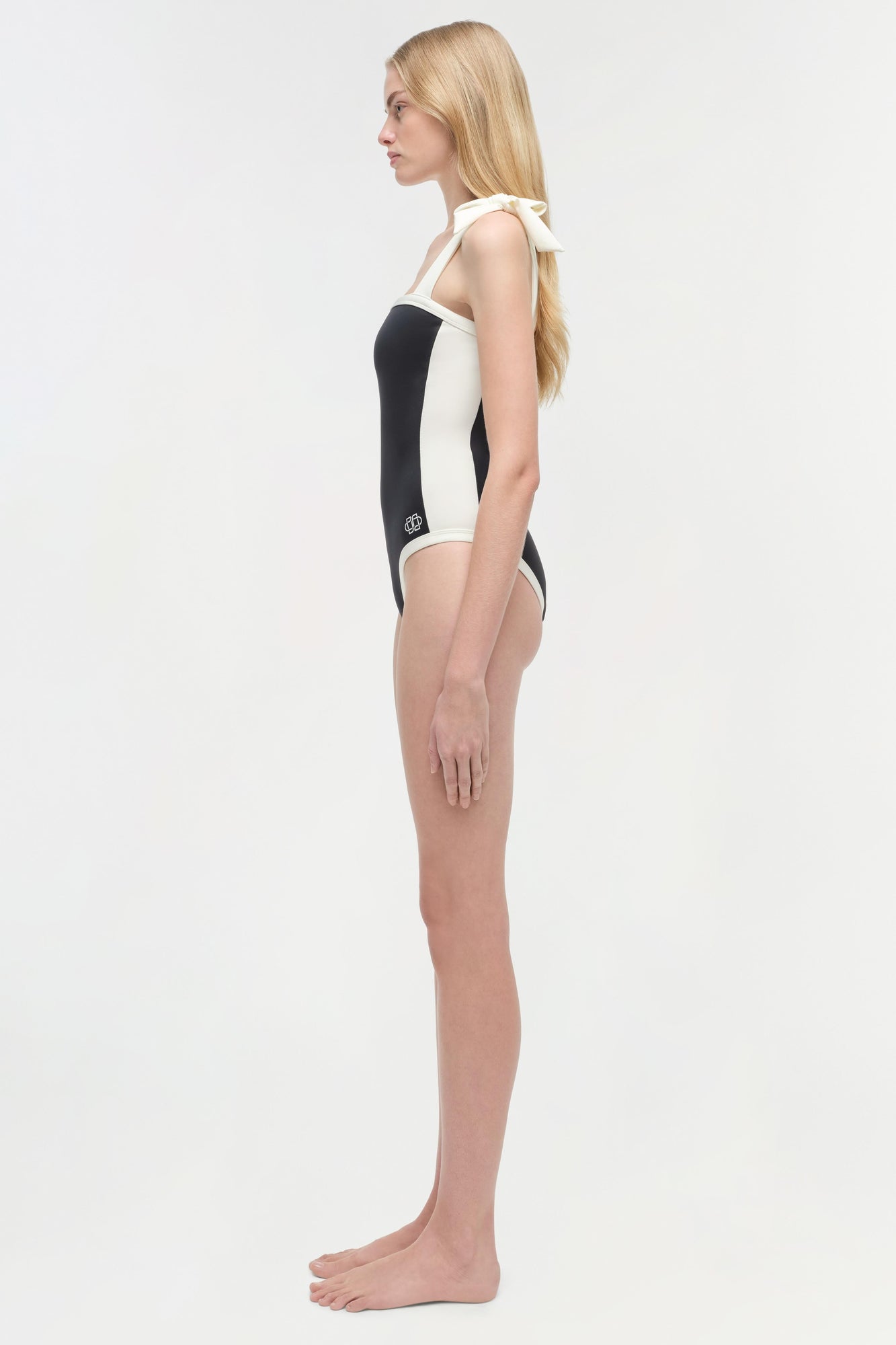 Woman wearing a black and white colorblocked one-piece swimsuit with halter neckline, shown from the side.
