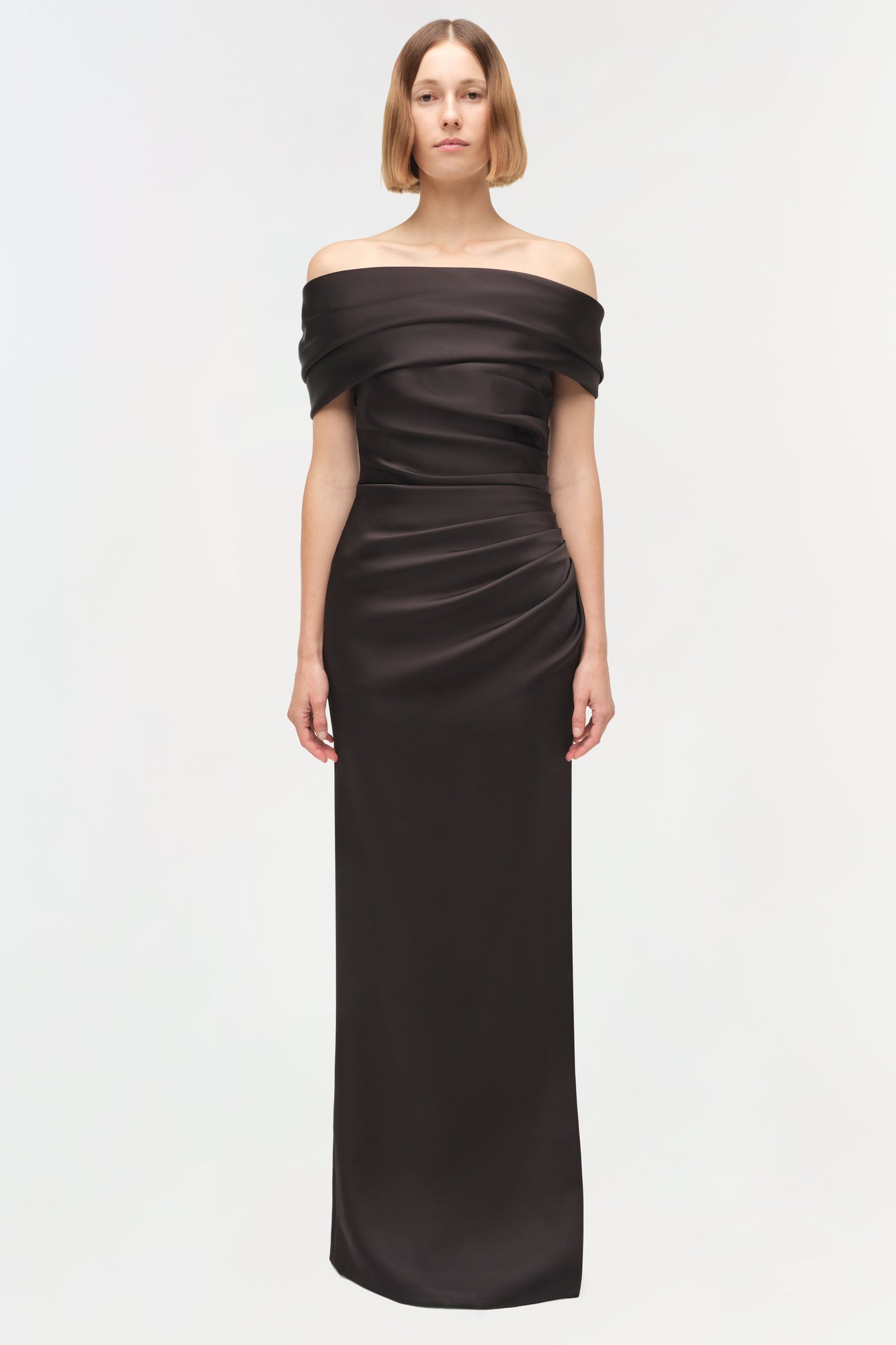 Black satin off-shoulder gown with draped neckline and ruched waist, floor-length silhouette.