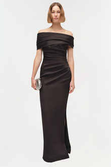 Black off-shoulder draped satin gown with ruched detailing and side slit, worn with metallic clutch.