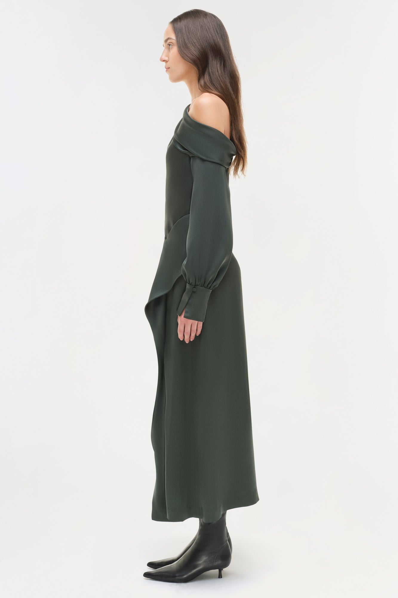 Woman wearing olive green satin midi skirt with off-shoulder long-sleeve top and black ankle boots, shown in profile view.