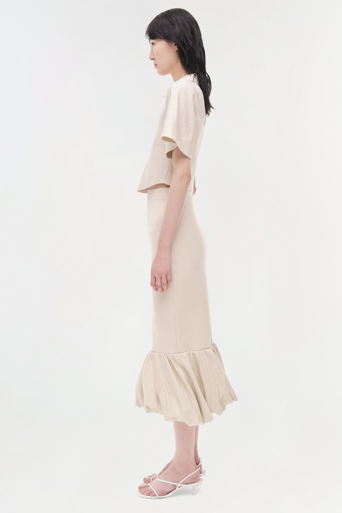 Cream linen knit midi skirt with ruffled hem, paired with matching short-sleeve top on model.