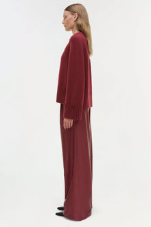 Woman wearing a burgundy crewneck cashmere sweater with pleated sleeves, shown in side profile.
