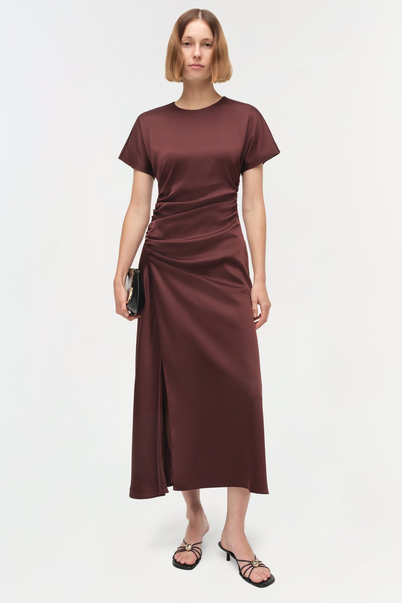 Burgundy satin midi dress with short sleeves, ruched side detailing, and a high slit, styled with black sandals.