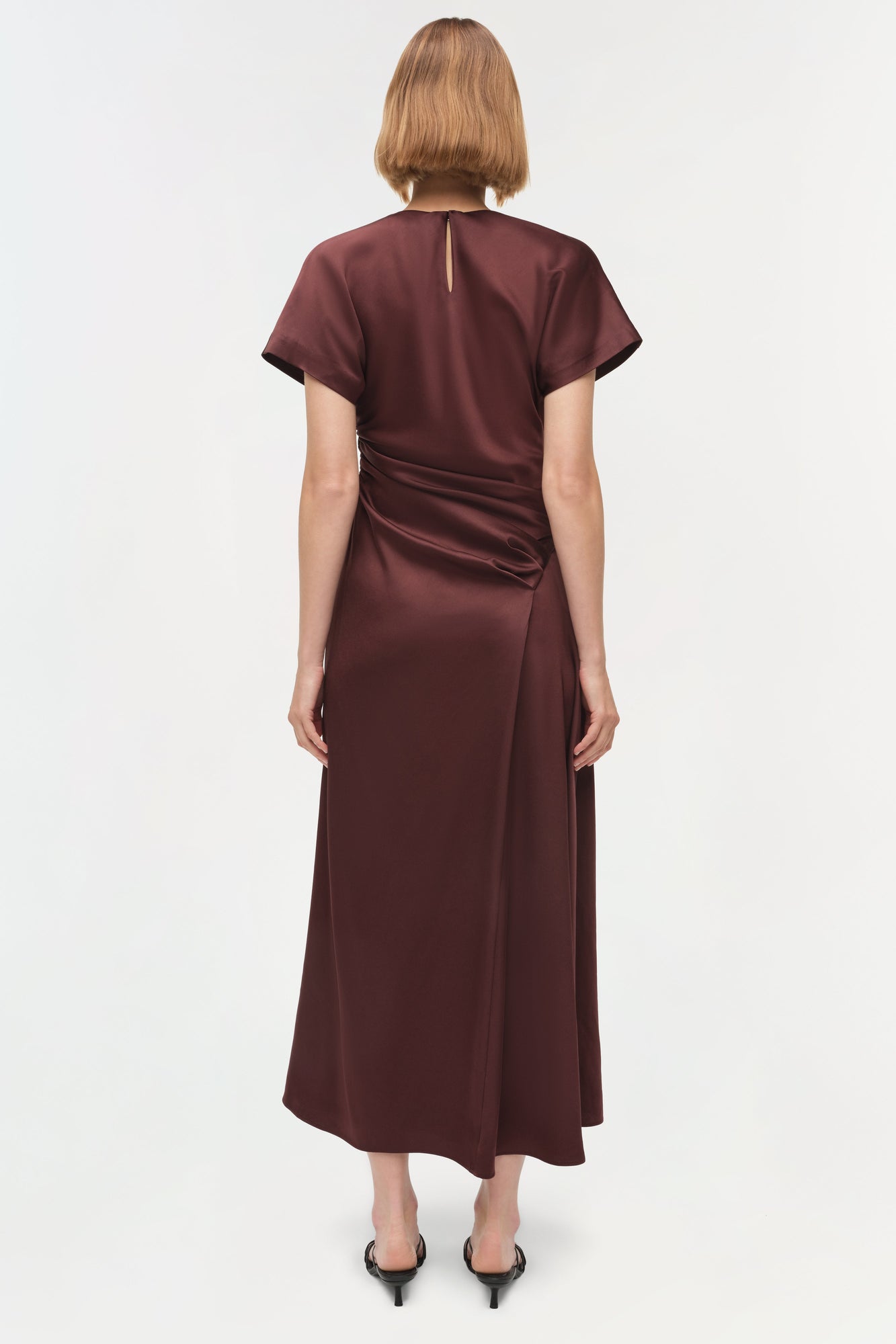 Burgundy satin midi dress with short sleeves and draped side ruching detail, shown from back view.