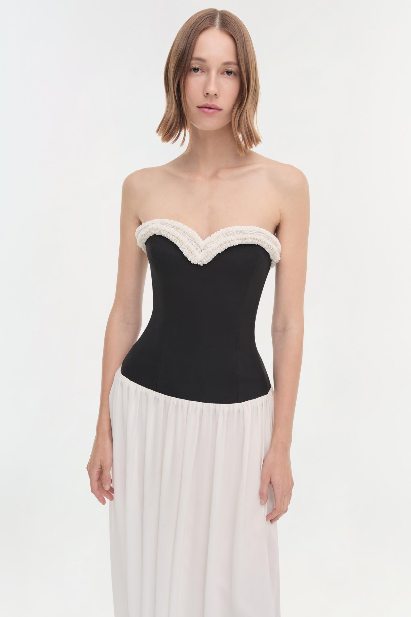 Woman wearing a strapless dress with a black corset bodice and white textured neckline trim, paired with a flowing cream skir
