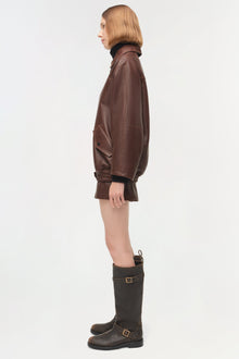 Brown leather oversized jacket with ribbed cuffs and collar, shown on model in side profile.