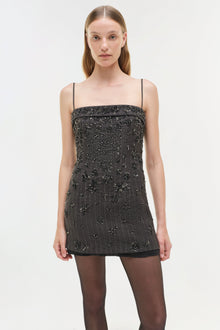 Black mini dress with silver beaded embellishments, thin straps, and straight neckline worn with dark tights.