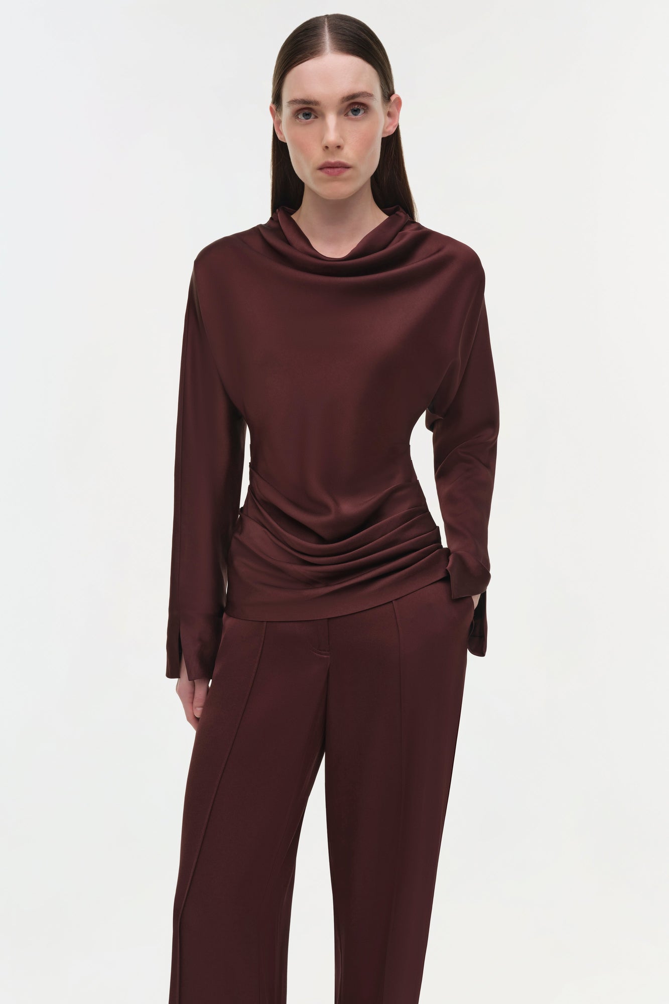 Burgundy draped satin top with cowl neckline and long sleeves on model wearing matching pants.