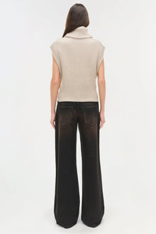Woman wearing beige sleeveless ribbed turtleneck and black wide-leg denim jeans, shown from back.