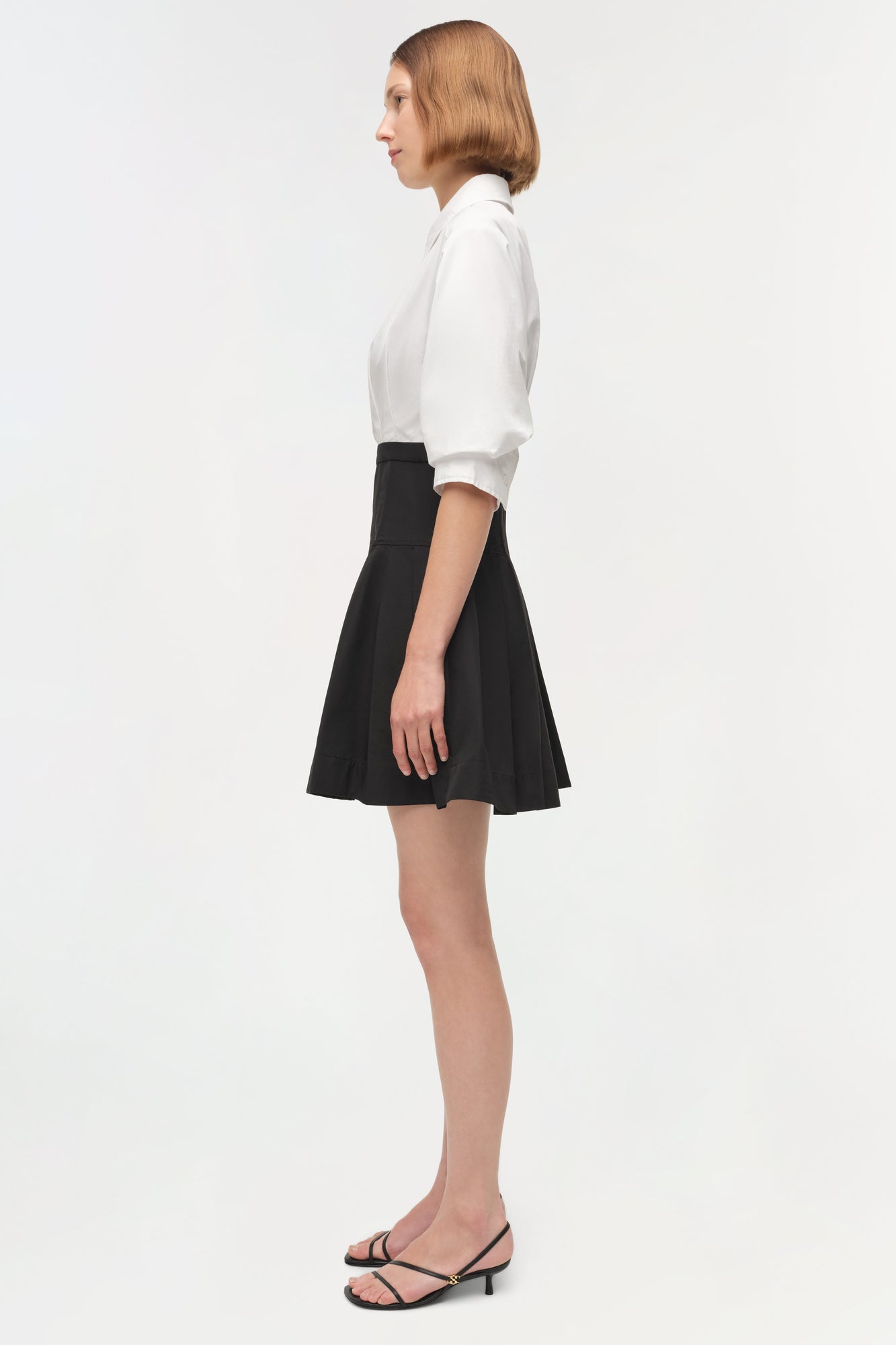 Woman wearing white collared shirt and black A-line mini skirt with black strappy heeled sandals.