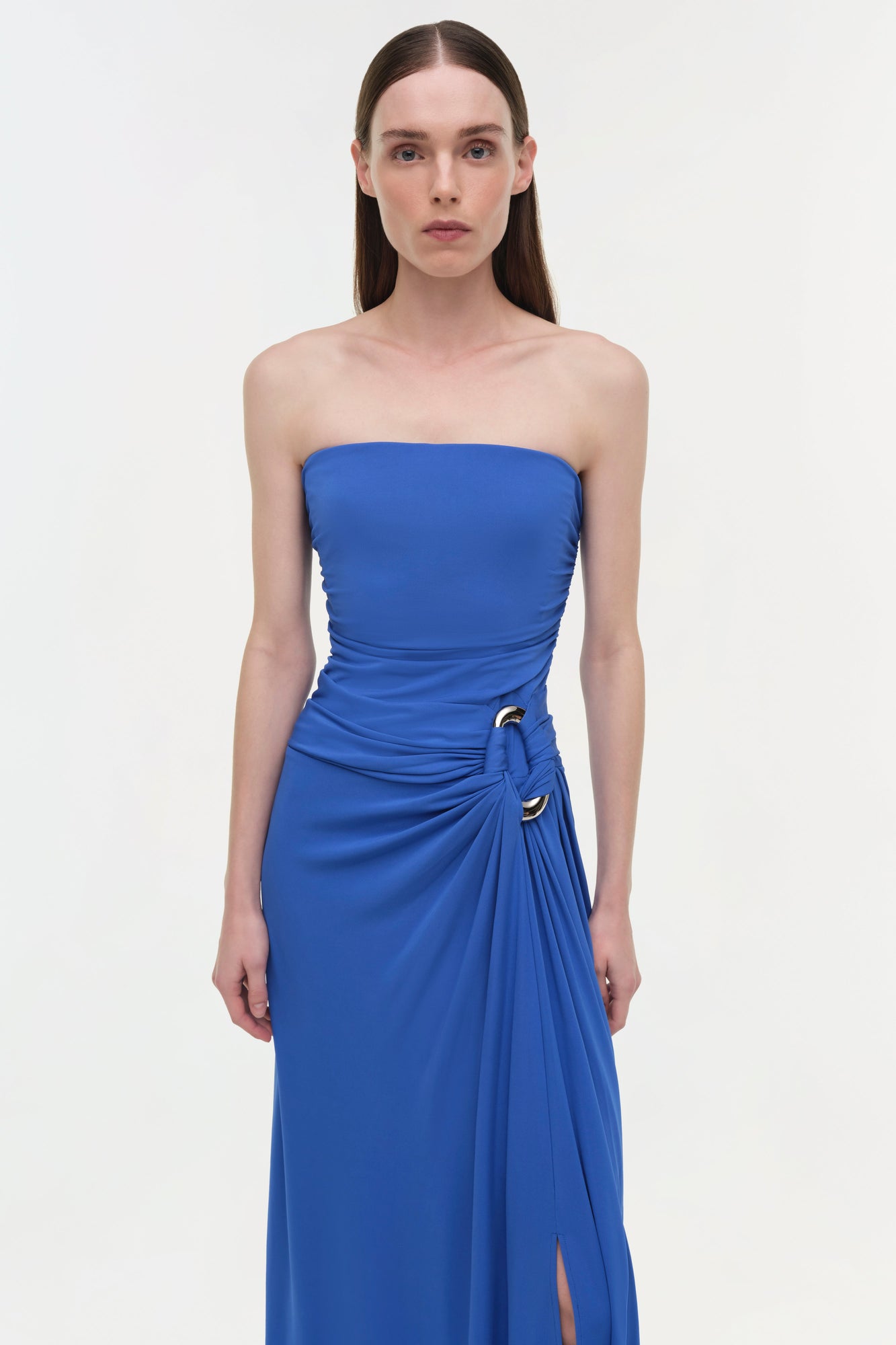 Blue strapless gown with draped ruching at waist and side slit, featuring gold hardware detail.