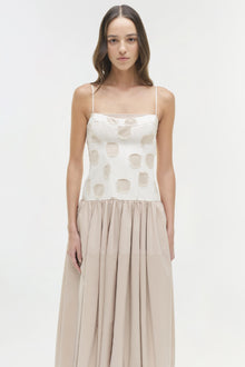Woman wearing white midi dress with circular cutout pattern on bodice and beige gathered skirt.
