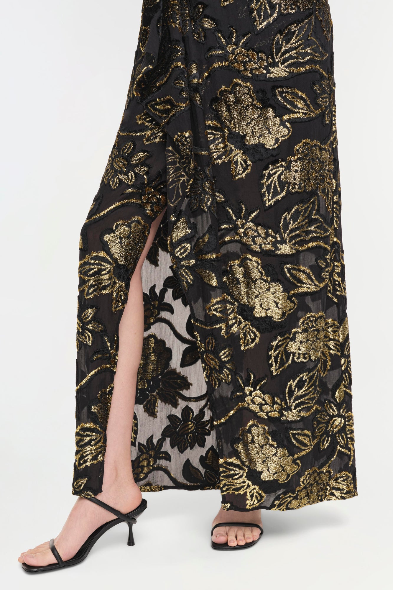 Black gown with gold floral embroidery and front slit, paired with black strappy heeled sandals.
