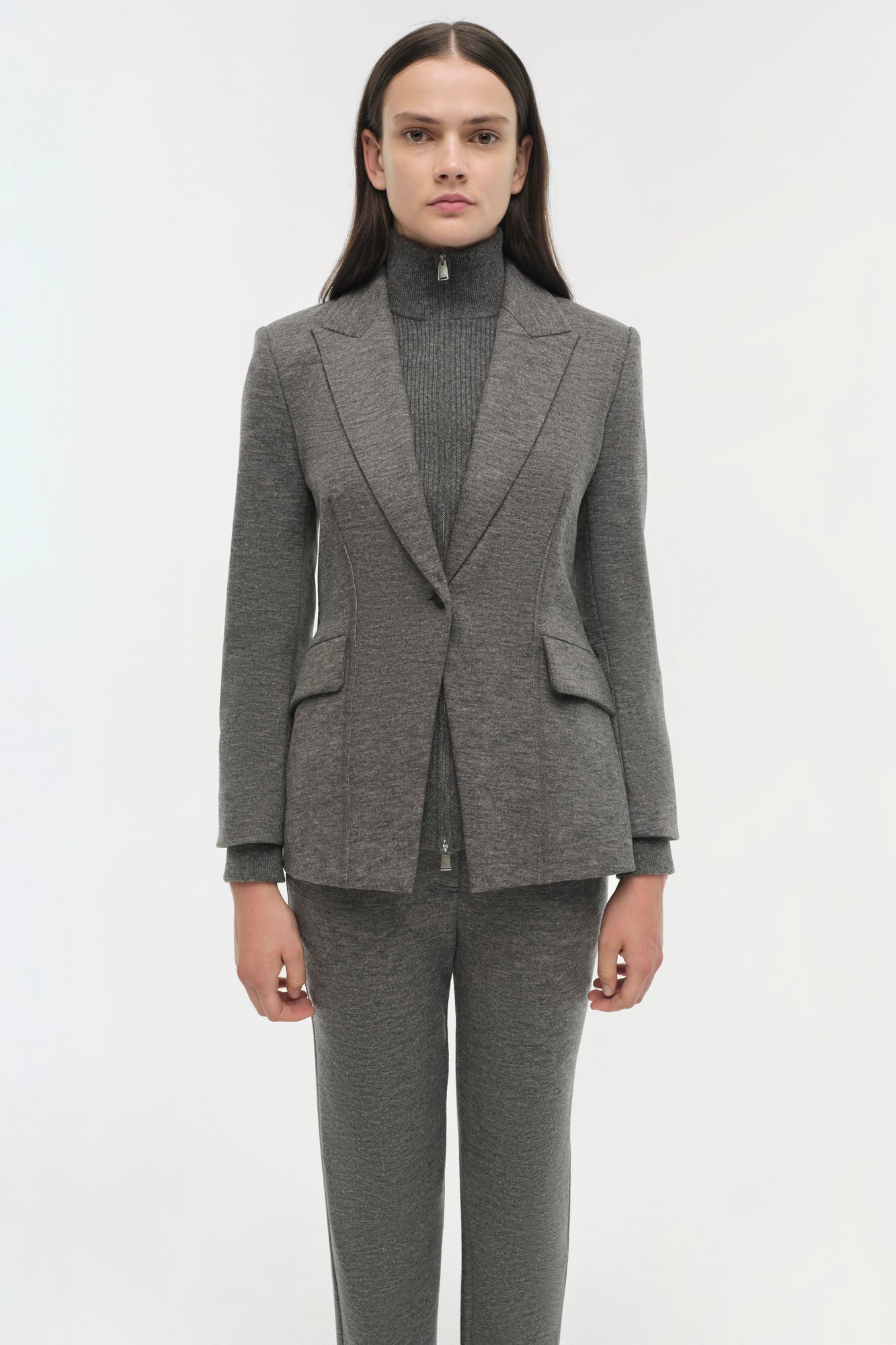 Gray wool blazer with notch lapels, single button closure, and flap pockets worn over matching ribbed turtleneck and trousers
