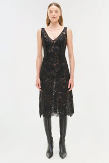Black sequin lace sleeveless midi dress with V-neckline worn with black knee-high boots.